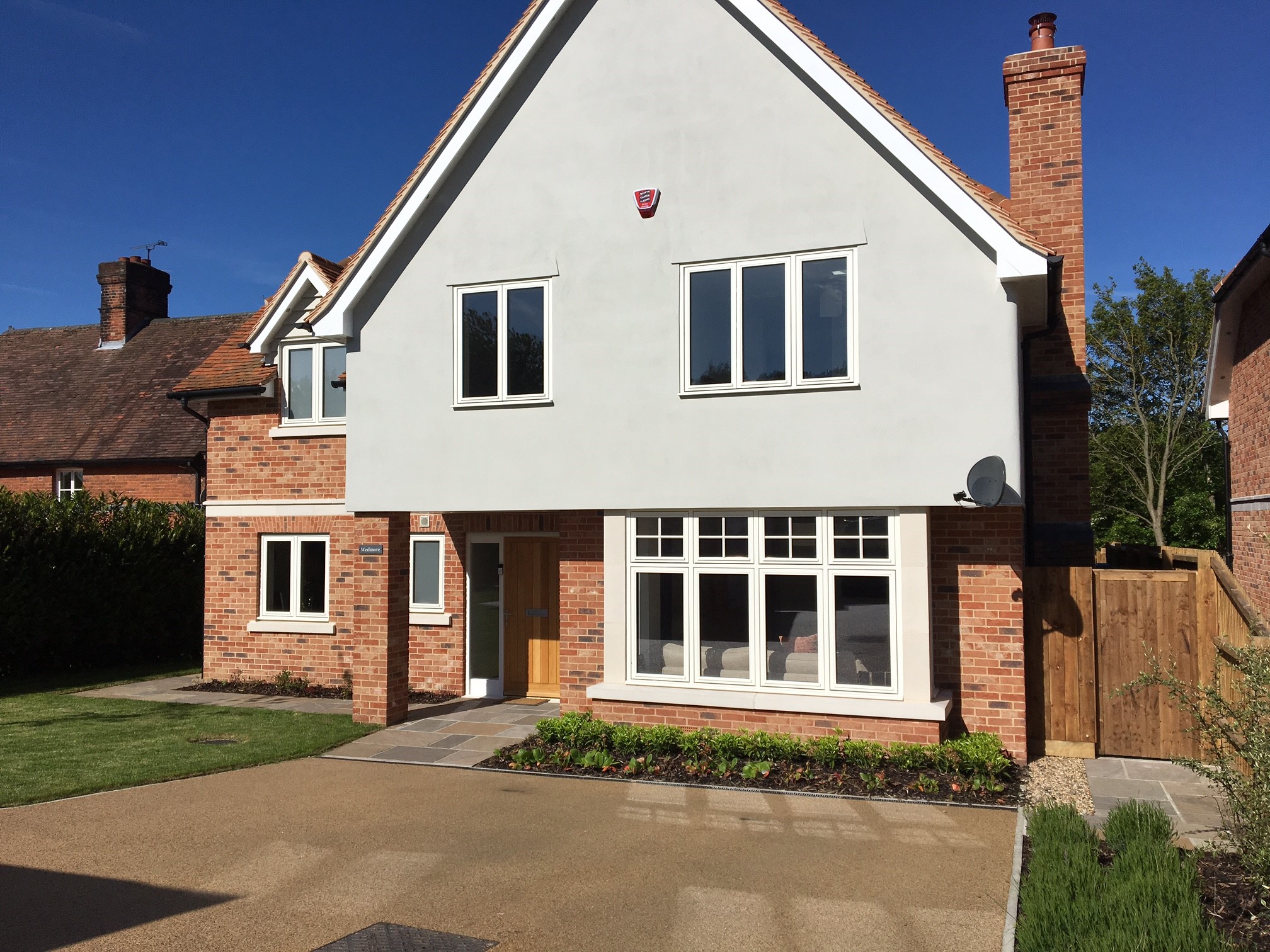 A large, modern two-story house with a light grey rendered upper floor and red brick lower floor, featuring numerous white timber casement windows.