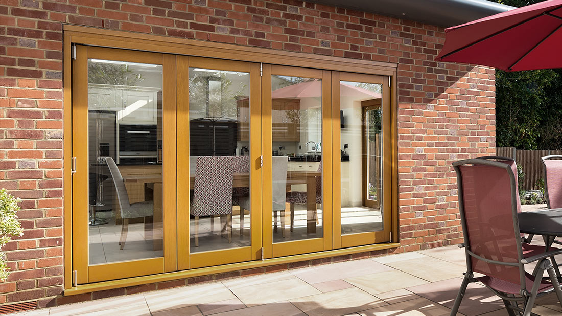 A modern home's exterior with wide wooden bi-fold patio doors leading to a paved outdoor area.